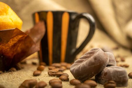 Fresh cupcake, coffee mug, chocolates and coffee beans on a homespun fabric with a rough texture. Close upの写真素材