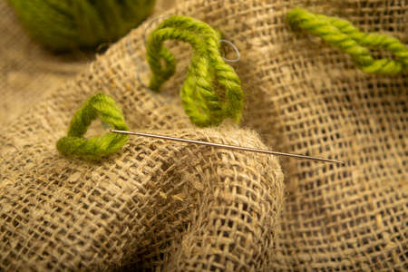 The girl stitches together pieces of coarse-textured burlap with green threads. Close upの写真素材