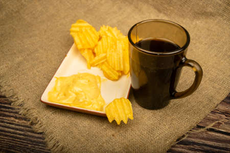 Potato chips with cheese sauce and a coffee mug on a wooden background. Close upの写真素材