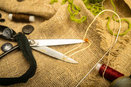 Buttons of various sizes, a spool of thread, tailor's scissors, and a zipper on rough-textured burlap. Close upの写真素材