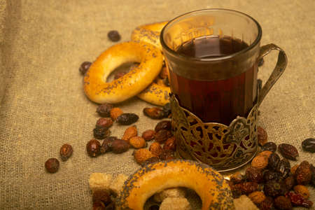 A cut glass of tea in a vintage Cup holder, chunks of brown cane sugar, small bagels and dried rosehip fruit scattered on a homespun cloth with a rough texture. Close upの写真素材