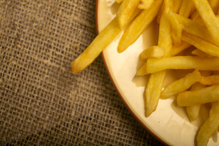 French fries in a round plate on a homespun cloth with a rough texture. Close up