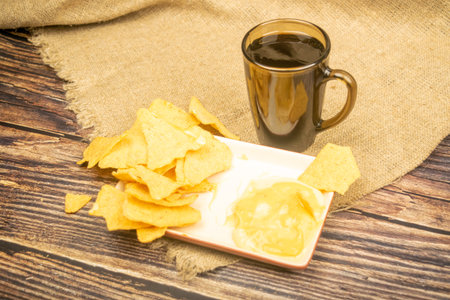 Corn chips with cheese sauce and a coffee mug on a wooden background. Close up