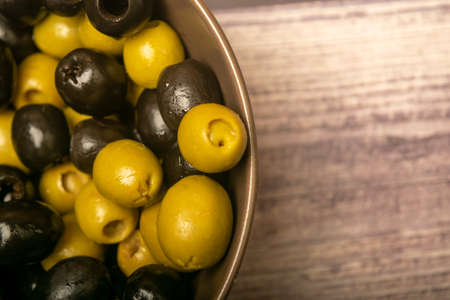 Green olives and black olives in a ceramic bowl on a wooden background. Close upの写真素材