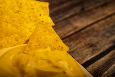 Corn chips with cheese sauce on a wooden background. Close up