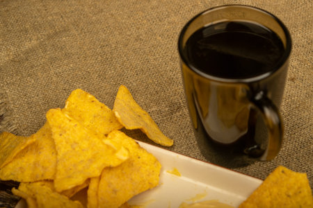 Corn chips with cheese sauce and a coffee mug on a wooden background. Close up