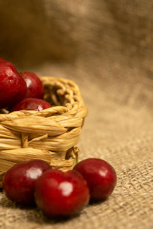 Ripe juicy cherries in a wicker basket and cherries scattered on a homespun fabric with a rough texture. Close upの写真素材