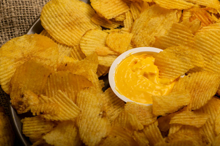 Fluted potato chips in a round plate with sauce in a saucepan in the middle of the plate on a...