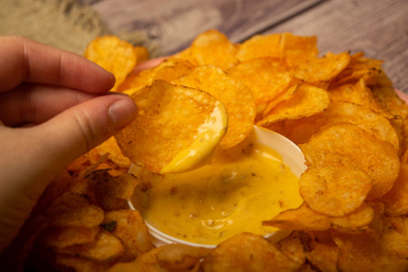 The girl takes a chip from a round dish with potato chips and a saucepan with cheese sauce in the...