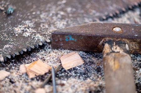 Old vintage hammer, wood saw, nails and sawdust on a wooden background, close-up, selective focusの写真素材