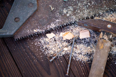 Old vintage hammer, wood saw, nails and sawdust on a wooden background, close-up, selective focusの写真素材