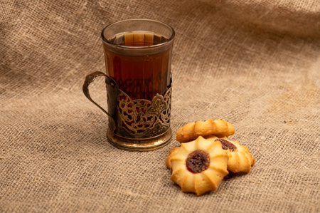 Homemade pastry cookies with jam and a faceted glass of tea in a vintage Cup holder on a background...