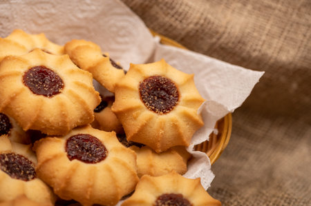 Homemade pastry cookies with jam in a wicker basket on a background of homespun fabric with a rough...