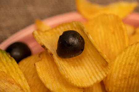 Crispy, delicious potato chips with mustard sauce and olives on a coarse homespun cloth. Close up