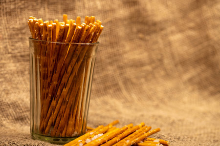 Salty bread strips in a glass cup and scattered on a background of coarse homespun fabric. Close-up,...