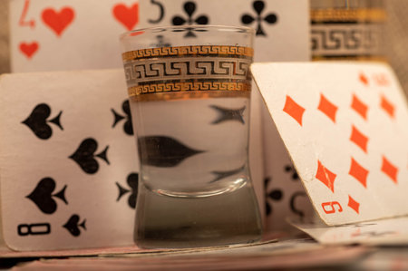 Playing cards and a glass of vodka on a table covered with coarse burlap. Close-up, selective focus.