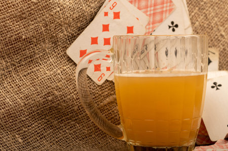 Playing cards and a mug of light unfiltered beer on a table covered with coarse cloth. Close-up,...