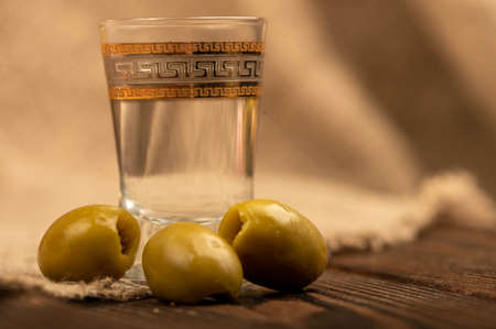 A glass of vodka and salted olives on a background of homespun fabric with a rough texture. Close-up Selective focusの写真素材