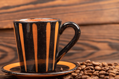 Roasted coffee beans scattered on a wooden surface and a coffee cup with a saucer close-up, selective focusの写真素材