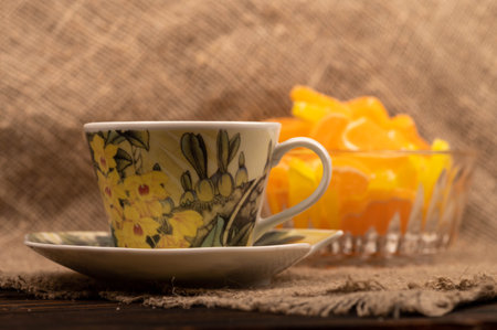Multicolored shaped marmalade lemon slices in a glass vase and a cup of tea on a saucer, close-up, selective focusの写真素材