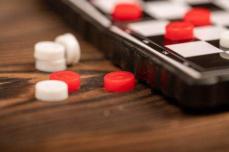 A board for playing checkers with chips on a wooden table, close-up, selective focus