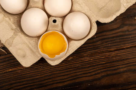 White chicken eggs and one broken egg in a tray made of white cardboard, close-up selective focusの写真素材