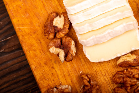 Sliced camembert and walnut kernels on a wooden cutting board, close-up, selective focusの写真素材