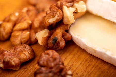 Sliced camembert and walnut kernels on a wooden cutting board, close-up, selective focusの写真素材