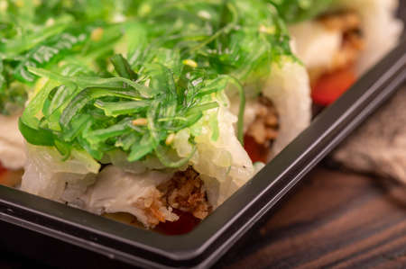 Delicious sushi roll with Philadelphia cheese, cucumber, salmon and chuka in a plastic tray on a wooden tableの写真素材