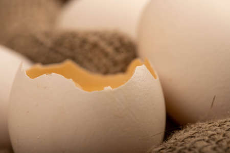 A broken white chicken egg and several whole eggs on a homespun fabric with a rough texture, close-up selective focusの写真素材