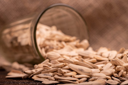 White sunflower seeds scattered and a faceted glass on the background of coarse burlap, close-up selective focusの写真素材