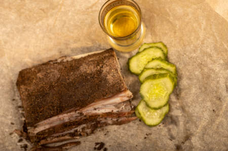 A piece of homemade bacon with pepper, a glass of homemade moonshine and chopped pickles close-up, selective focusの写真素材