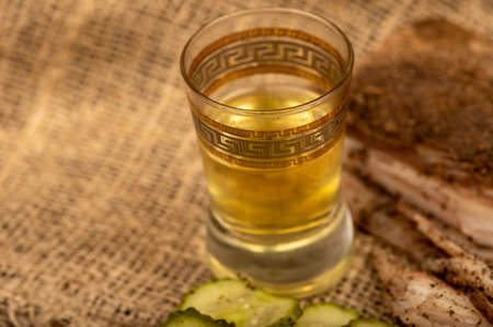 A piece of homemade bacon with pepper, a glass of homemade moonshine and chopped pickles close-up, selective focusの写真素材