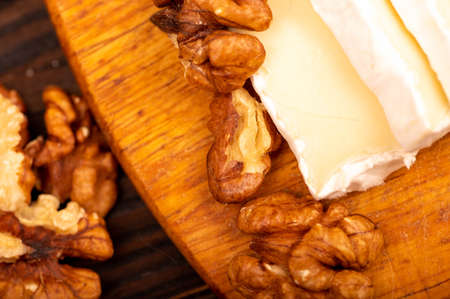 Sliced camembert and walnut kernels on a wooden cutting board, close-up, selective focusの写真素材
