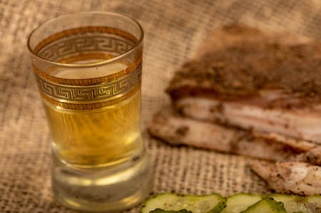 A piece of homemade bacon with pepper, a glass of homemade moonshine and chopped pickles close-up, selective focusの写真素材