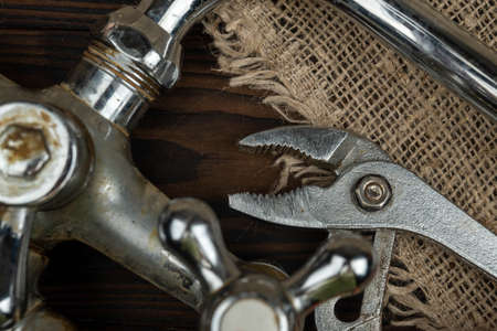 A wrench and an old bathroom faucet on a wooden tableの写真素材