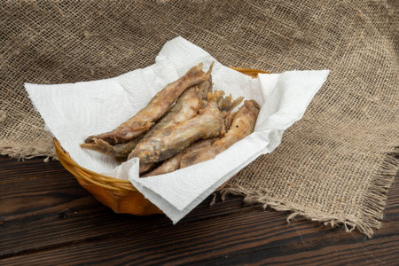 Fried fish on a paper napkin in a wicker basket on a wooden table