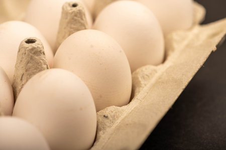 White chicken eggs in a tray made of white cardboard, close-up selective focus
