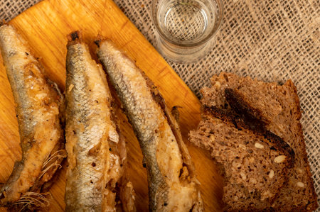 A small fried fish on a wooden board, pieces of bread and a glass of vodka, close-up, selective focusの写真素材