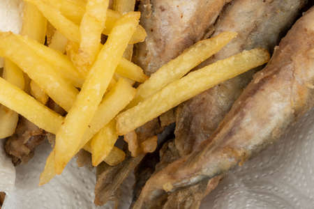 Fried fish and French fries on a paper napkin in a wicker basket on a wooden tableの写真素材