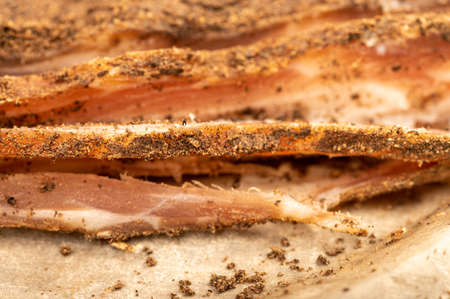 A piece of homemade bacon with pepper on white oiled paper, close-up, selective focusの写真素材