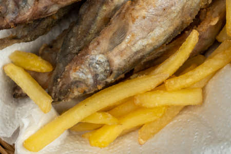 Fried fish and French fries on a paper napkin in a wicker basket on a wooden tableの写真素材