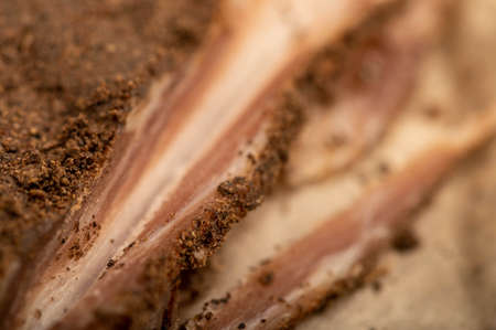 A piece of homemade bacon with pepper on white oiled paper, close-up, selective focusの写真素材