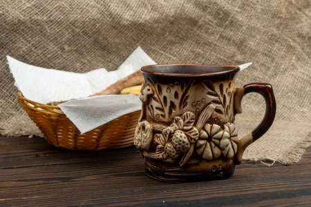 Fried fish and French fries on a paper napkin in a wicker basket and a mug of tea on a wooden tableの写真素材