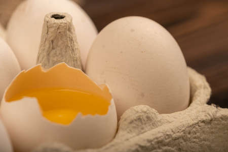 White chicken eggs and one broken egg in a tray made of white cardboard, close-up selective focusの写真素材