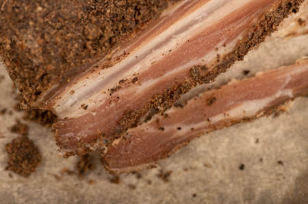 A piece of homemade bacon with pepper on white oiled paper, close-up, selective focusの写真素材