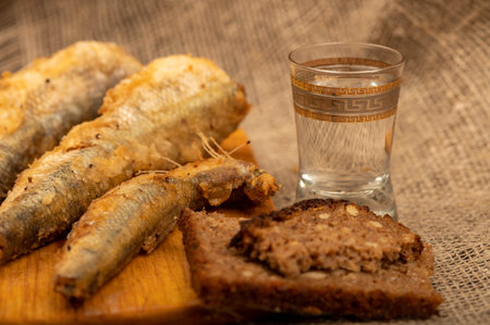 A small fried fish on a wooden board, pieces of bread and a glass of vodka, close-up, selective focusの写真素材