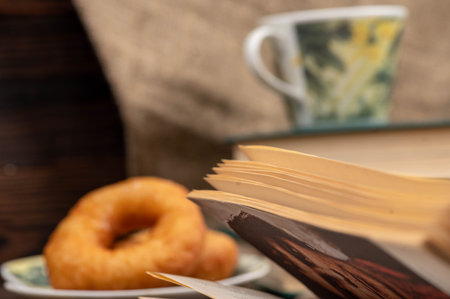 A cup of strong tea on a saucer, donuts on a plate and a stack of books on the table