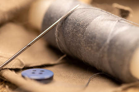 A spool of sewing thread and a sewing needle on a fabric background. Close-up, selective focus.の写真素材