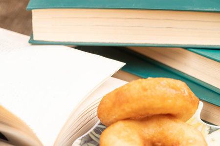 A cup of strong tea on a saucer, donuts on a plate and a stack of books on the table